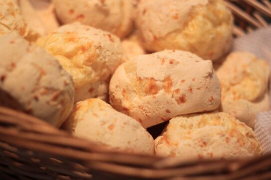 Uma imagem apetitosa de pão de queijo, um quitute tradicional da culinária brasileira, com sua textura dourada e crocante por fora, contrastando com o interior macio e recheado de queijo. Uma delícia popular no Brasil e além, perfeita para acompanhar um café fresco ou desfrutar como um petisco saboroso